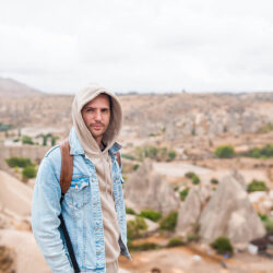 Homme portant une veste en jean avec un sac à dos dans un paysage rocailleux après avoir suivi un cours de français en ligne avec Edlingo.