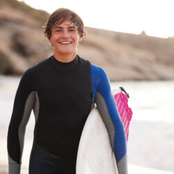 Jeune homme souriant avec une planche de surf après avoir suivi un cours d’anglais en ligne avec un tuteur Edlingo.