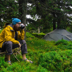 Homme buvant un café devant sa tente en pleine nature après avoir suivi un cours de français en ligne avec un tuteur Edlingo.