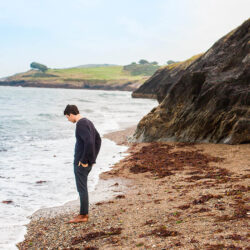 Homme debout sur une plage rocheuse contemplant l’océan après avoir suivi un cours d’espagnol en ligne avec un tuteur Edlingo.