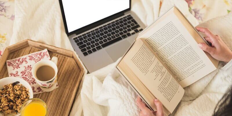 Personne lisant un livre avec un ordinateur à côté pour améliorer sa compréhension de l’anglais.