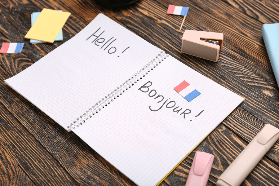Open notebook with the words Hello and Bonjour written alongside a French flag, representing essential beginner French words for daily life